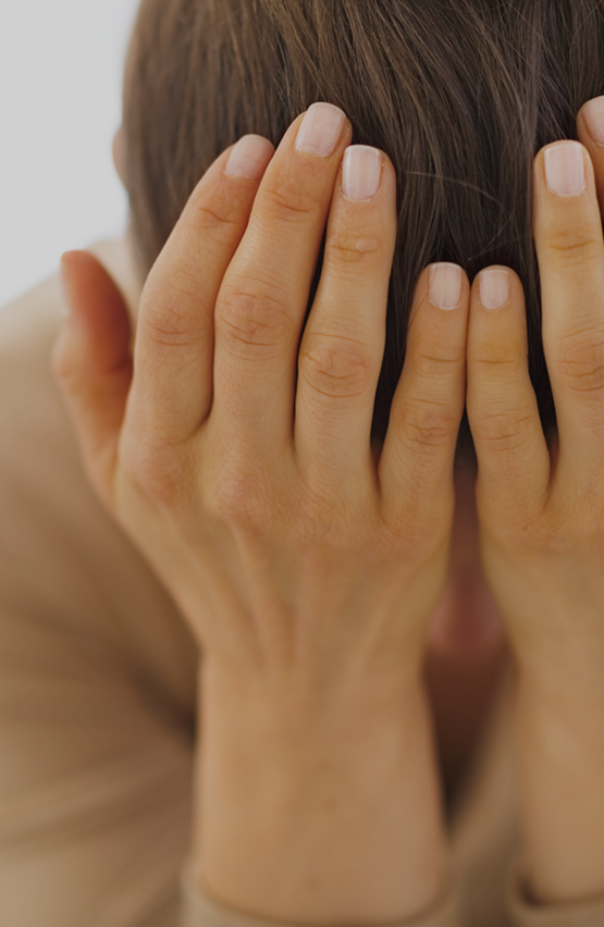 Person covering their face with both hands, suggesting stress, overwhelm, or emotional distress.